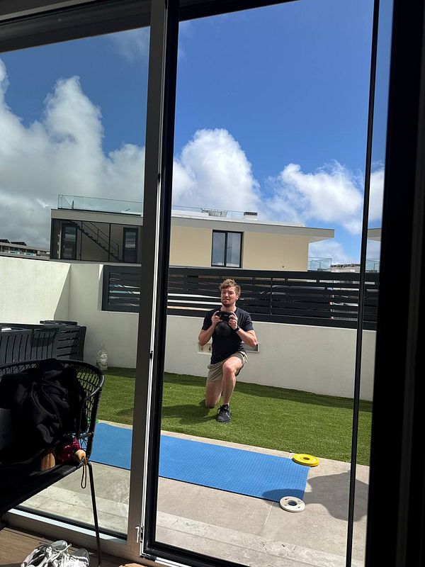 A man is exercising outdoors with a kettlebell in a backyard setting.