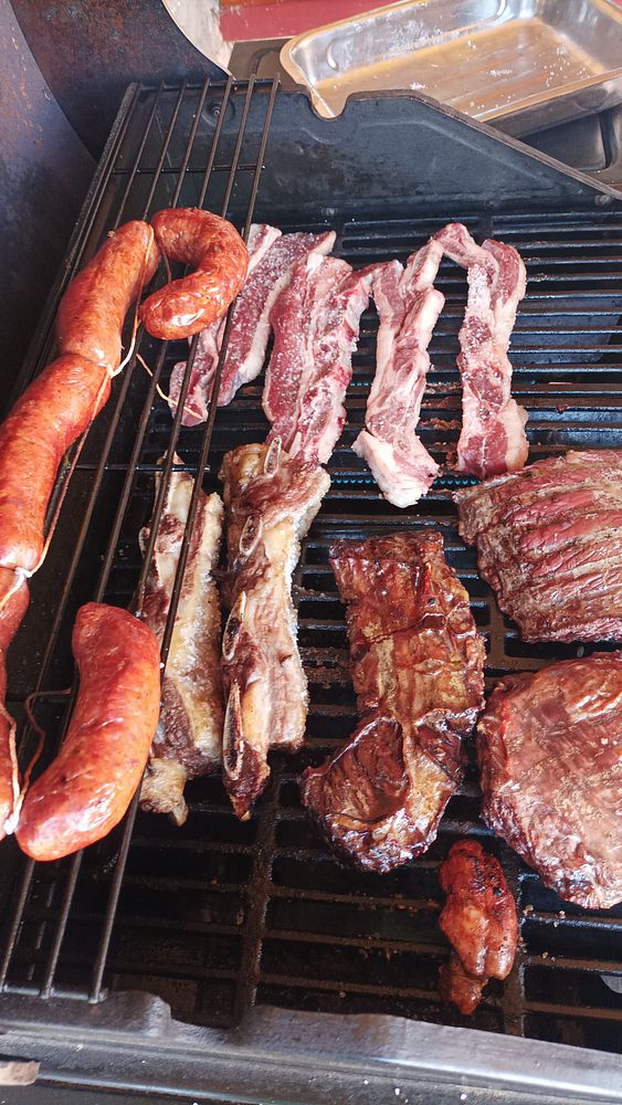 A sizzling Argentinean barbecue on a grill with two skewers of meat cooking over glowing charcoal flame.
