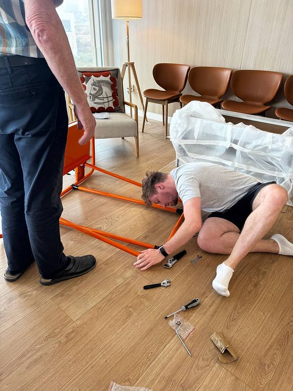 Two individuals are assembling a large orange carriage in a modern living space.