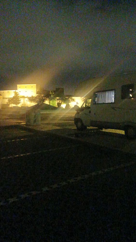 A parked camper van is illuminated by nearby lights in a nighttime setting in Portugal.