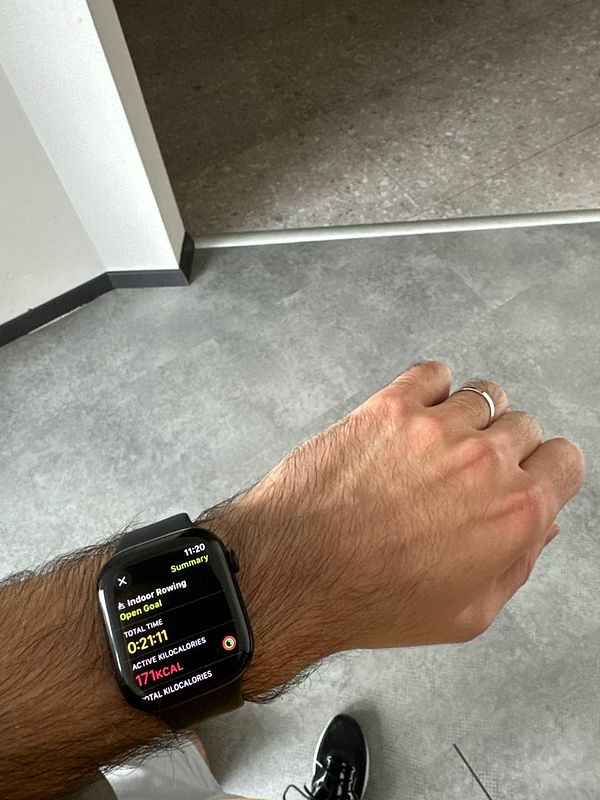A smartwatch displays workout statistics while a person prepares for indoor rowing.