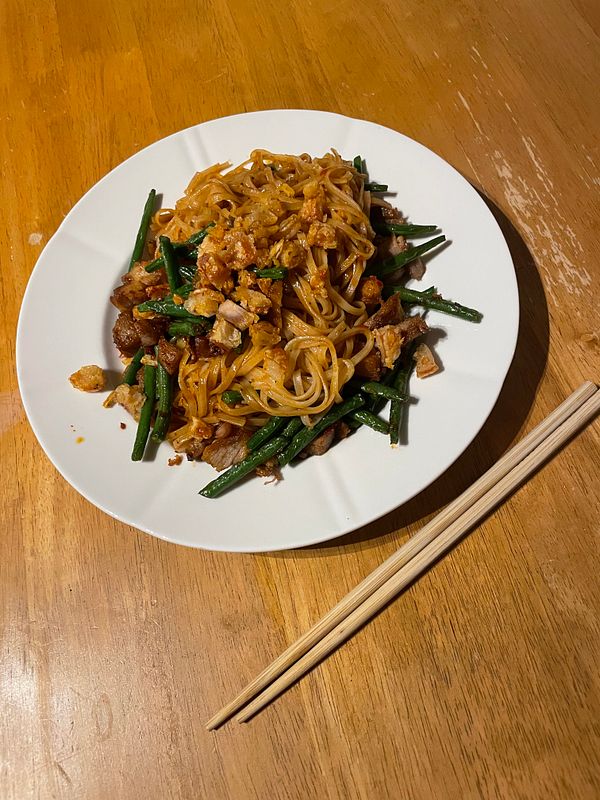 A plate of pork belly stir-fry with noodles and green beans is presented on a wooden table.
