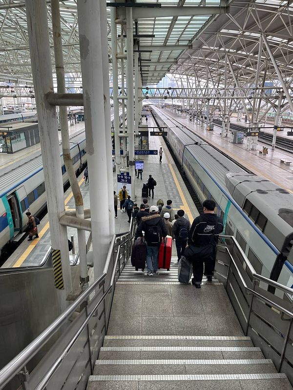 Passengers are descending stairs at a train station, preparing to board a train to Busan.