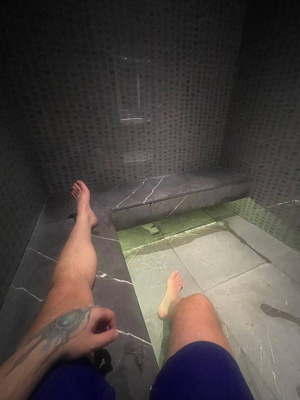 A person relaxing in a steam room with their feet in a shallow pool of water.