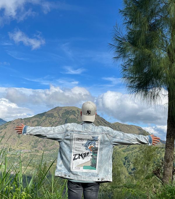 A person stands with arms outstretched against a scenic mountainous backdrop in Kintamani.