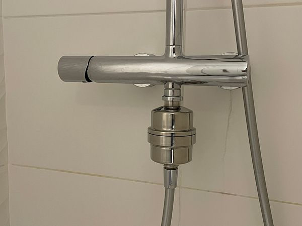 A close-up view of a chrome shower faucet with a water filter attachment.