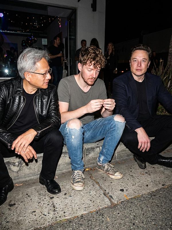 Three men are seated on a sidewalk at night, engaged in conversation.