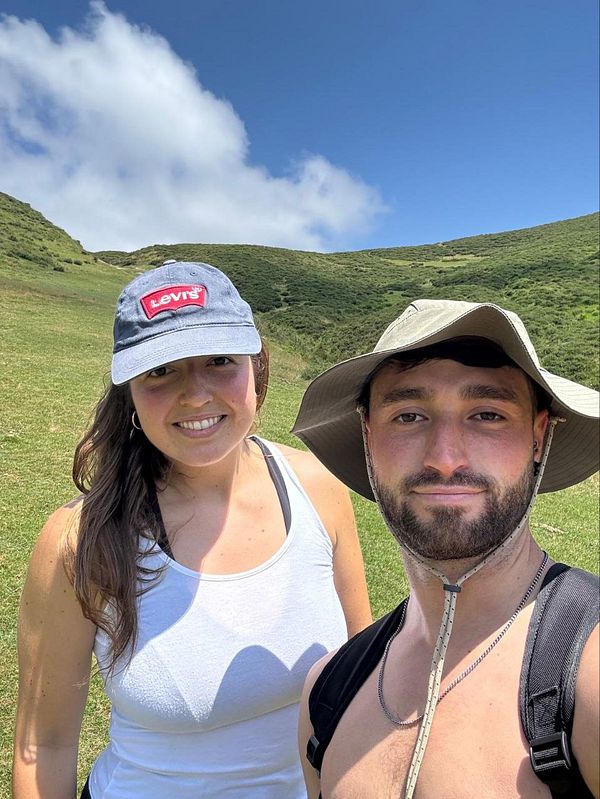 A woman and a man pose for a selfie during a hike in a lush green landscape.