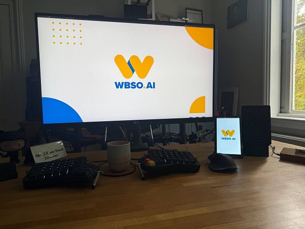 A workspace featuring a computer monitor and a mobile device displaying the WBSo.AI logo.