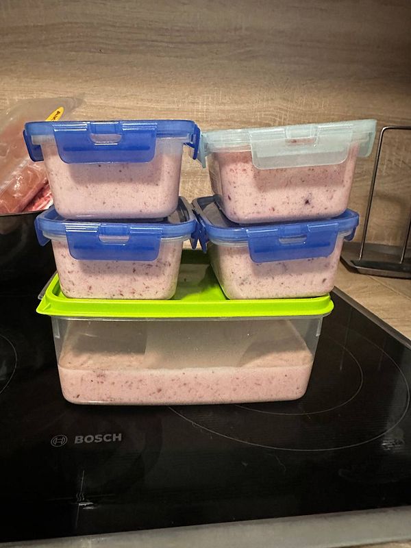 Four containers of homemade strawberry ice cream stacked on a kitchen countertop.