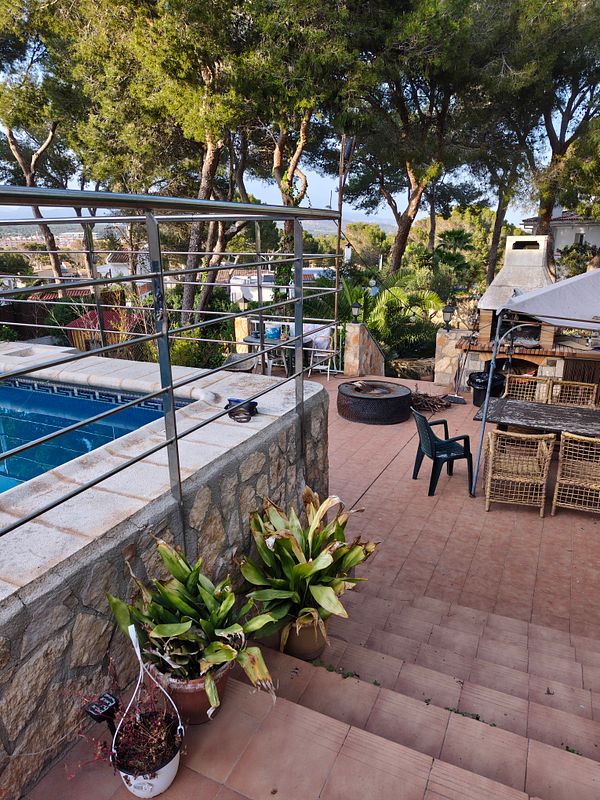 A cozy terrace setup with an iron table and chairs, plants, and garden furniture arranged for a BBQ gathering.
