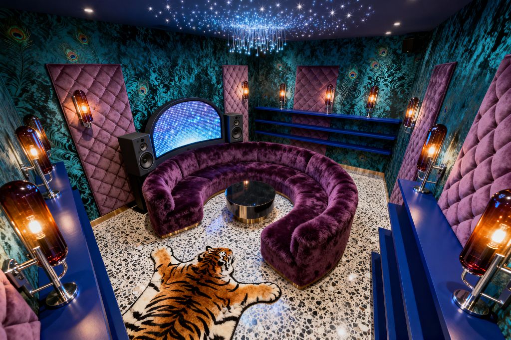 A maximalist media room features a plush semicircular purple velvet sofa around a black round coffee table on a speckled terrazzo floor with a tiger rug. Teal peacock-pattern flocked wallpaper and quilted purple acoustic panels flank a curved LED screen with tower speakers, while cobalt shelves and smoked-glass tube sconces in chrome line the walls; a navy ceiling with fiber-optic star lights and a sparkling pendant creates a theatrical lounge atmosphere.