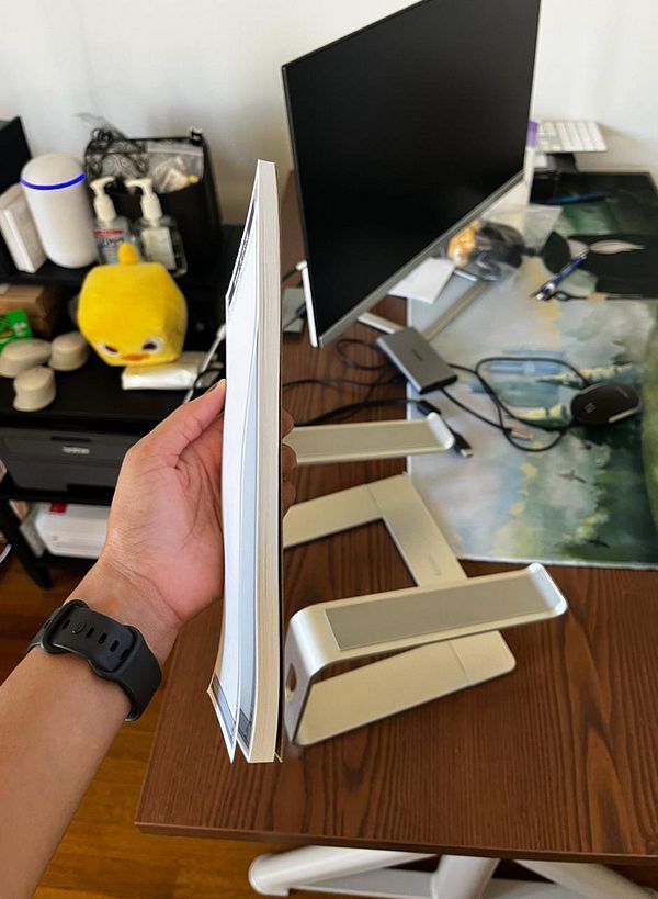 A person is holding a thick notepad next to a modern workspace setup.