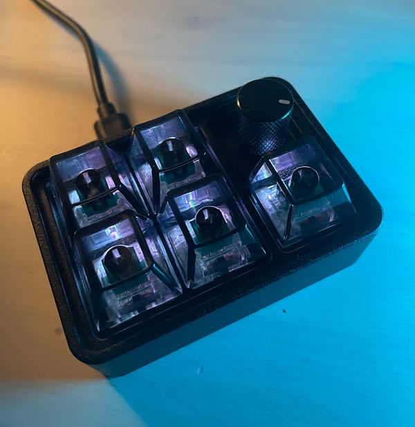 A compact mechanical keyboard with illuminated switches and a volume knob.