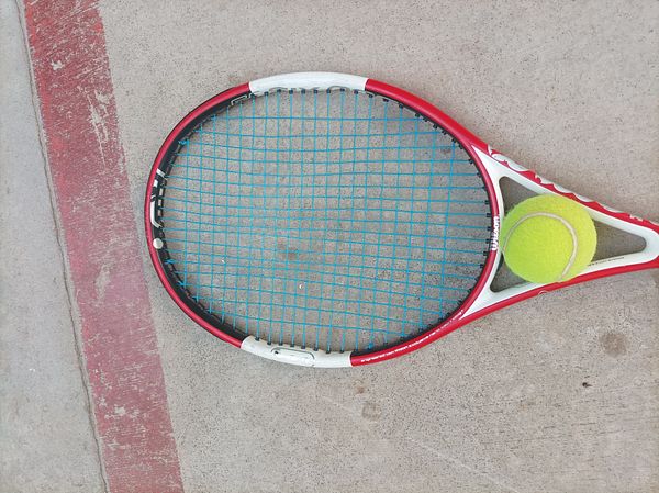 A tennis racket and a tennis ball are placed on a concrete surface.