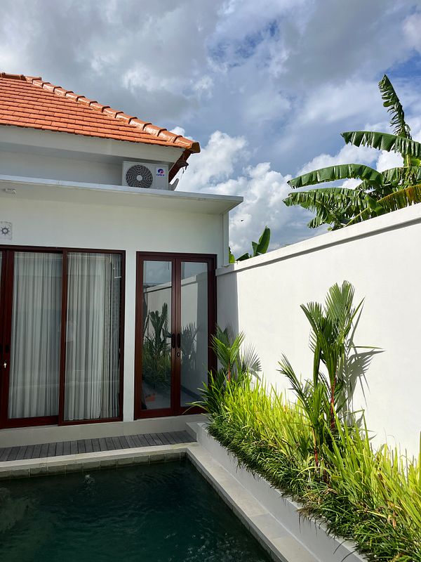 A serene outdoor space featuring a private pool, lush greenery, and a modern building.