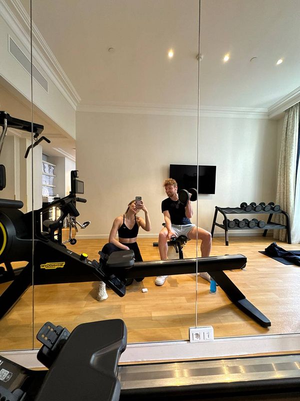A gym scene featuring two individuals taking a selfie in a well-equipped fitness room.
