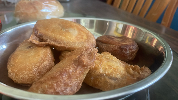 A close-up view of freshly fried banana fritters in a metal bowl.