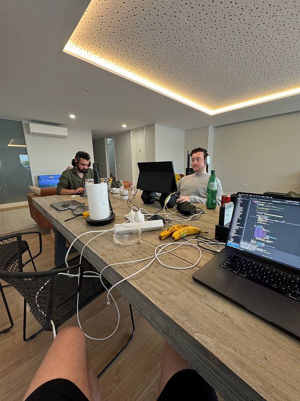 A coworking space featuring two individuals working at a table with laptops and various items.