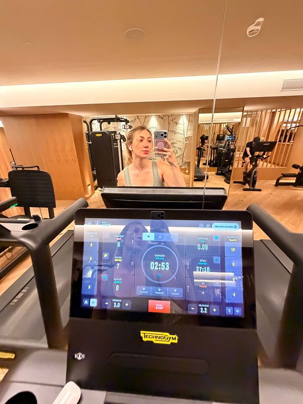 Photo of a woman stretching in a gym workout room with exercise equipment in the background.