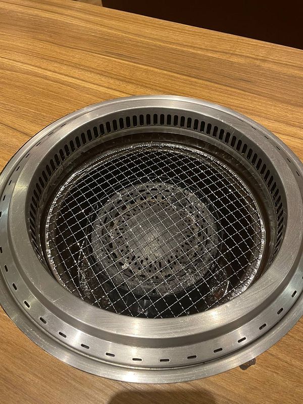 A tabletop grill featuring various cuts of meat being cooked, surrounded by plates and side dishes in a yakiniku meal setting.