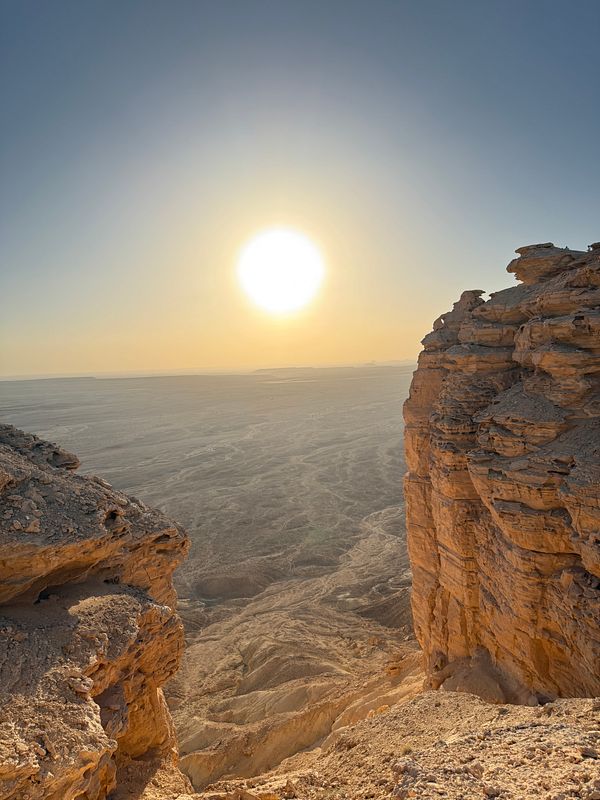 A breathtaking view from a rocky cliff overlooking a vast desert landscape at sunset.