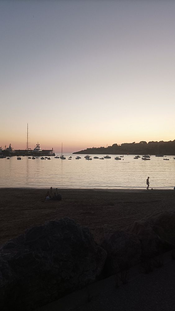 A serene beach scene at sunset with boats in the water and people enjoying the view.