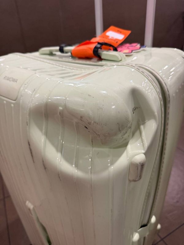 A damaged silver Rimowa suitcase with multiple dents and scratches on its surface.