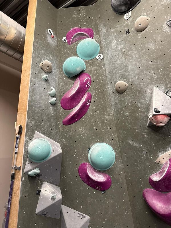 A person bouldering indoors on a climbing wall with colorful holds and a cushioned floor beneath.