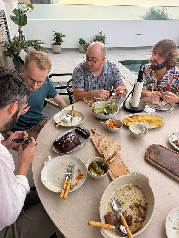 Four men sitting around a table outdoors, finishing a meal with various dishes and bread on the table.