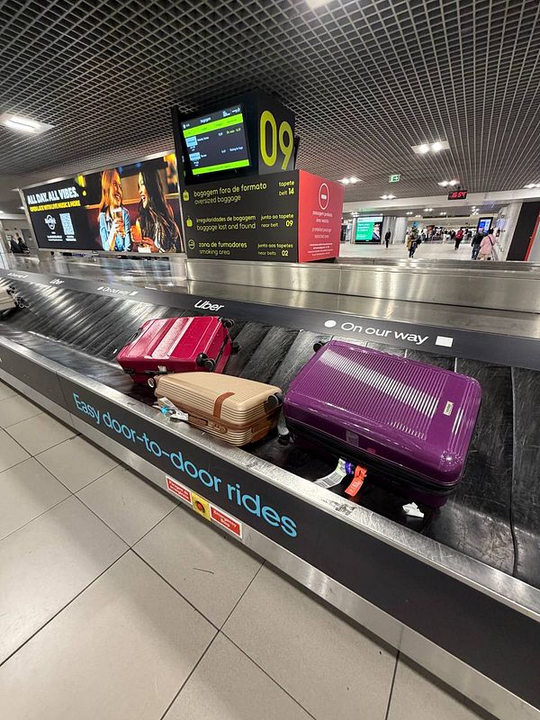 Baggage claim area at Lisbon Airport with malfunctioning luggage carousel and three suitcases stuck on the belt.
