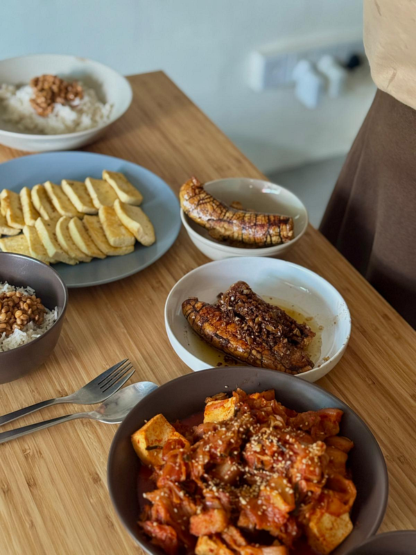 A kitchen scene showing two people preparing food on a wooden countertop with various fresh ingredients and cooking utensils.