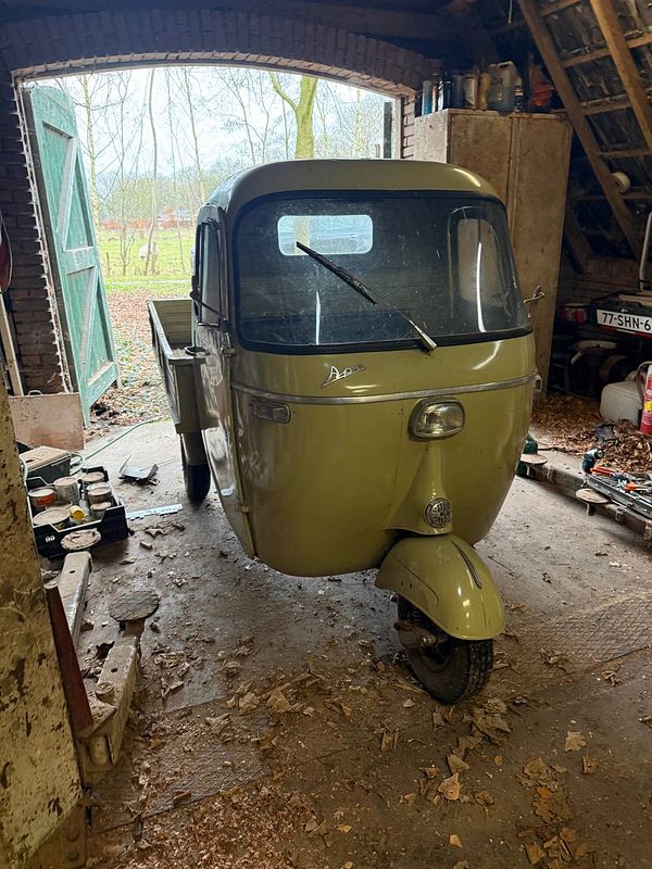 A classic dark green Volkswagen Beetle with its hood open, parked in a residential driveway.