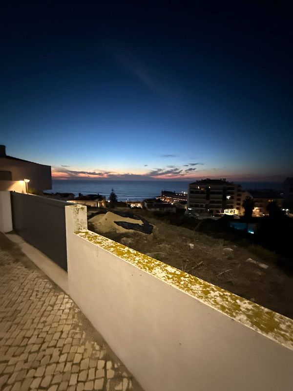 A scenic view of the ocean at dusk, framed by a wall and cobblestone pathway.