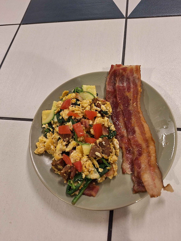 A plate of colorful egg scramble accompanied by crispy bacon.