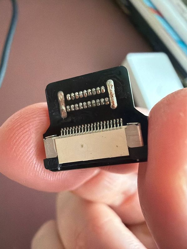 A close-up image of a connector being held between fingers.