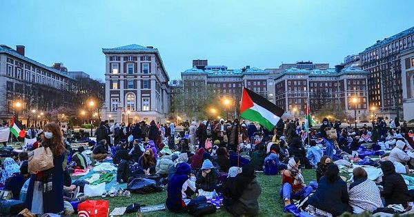 A large gathering of people participating in a protest, with flags and a historic building in the background.