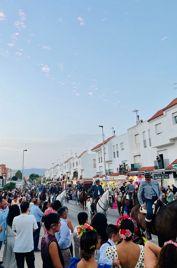 A lively street scene during the Feria de Caballos, featuring a parade of horse riders and a large crowd of spectators.