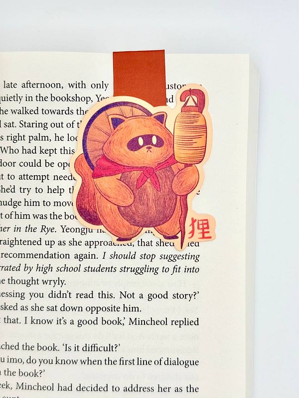 A colorful magnetic bookmark featuring a cartoon cat character is placed in an open book.