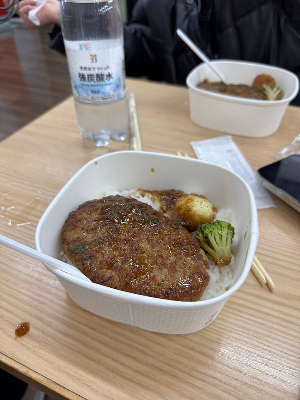 A meal from 7/11 featuring a meat patty served over rice with vegetables.