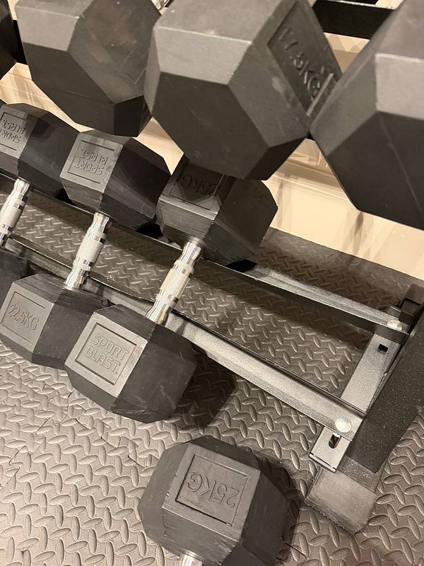 A broken gym dumbbell rack with twisted metal causing a dumbbell to fall off.