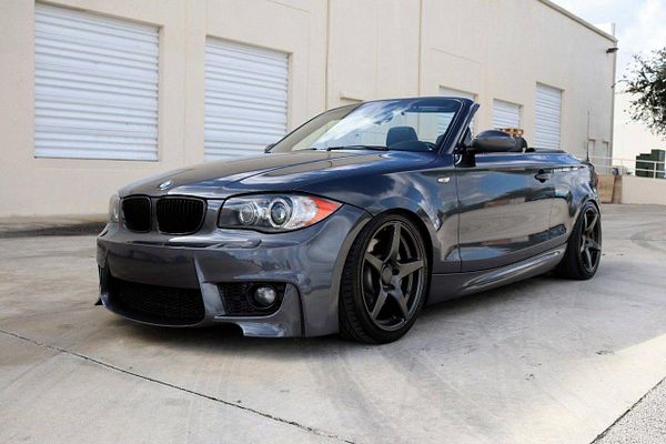 Silver BMW sedan parked on a gravel road near green shrubbery under a bright blue sky with scattered clouds.