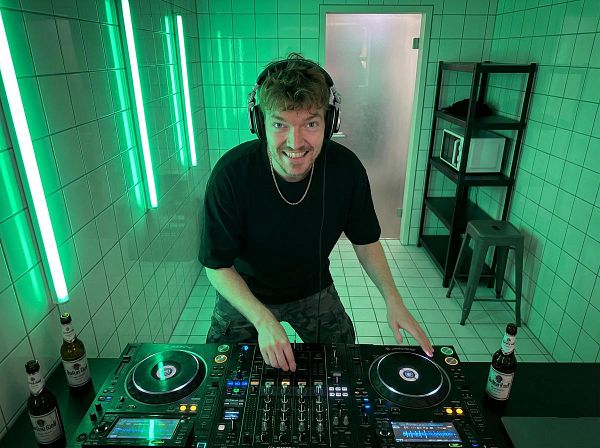 A DJ is performing in a modern, tiled room illuminated with green lighting.