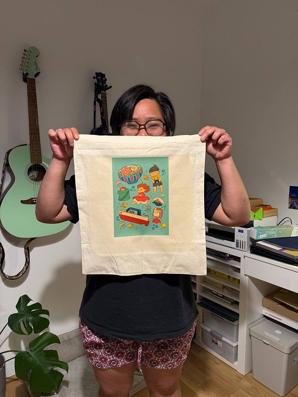 A person holds up a printed tote bag featuring colorful illustrations.