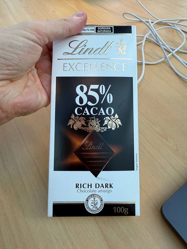 A photo of an opened 70% dark chocolate bar with a shiny foil wrapper on a greyish wooden surface.