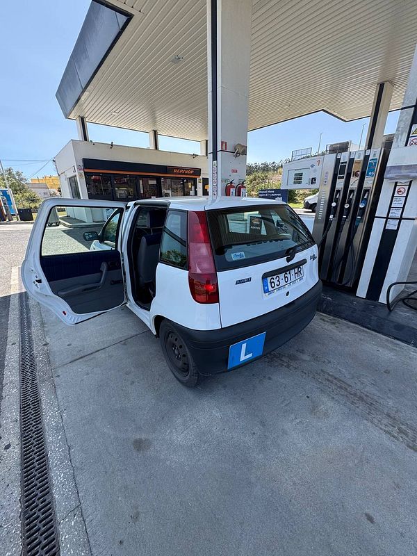 A white car with a learner's plate is parked at a gas station with its door open.