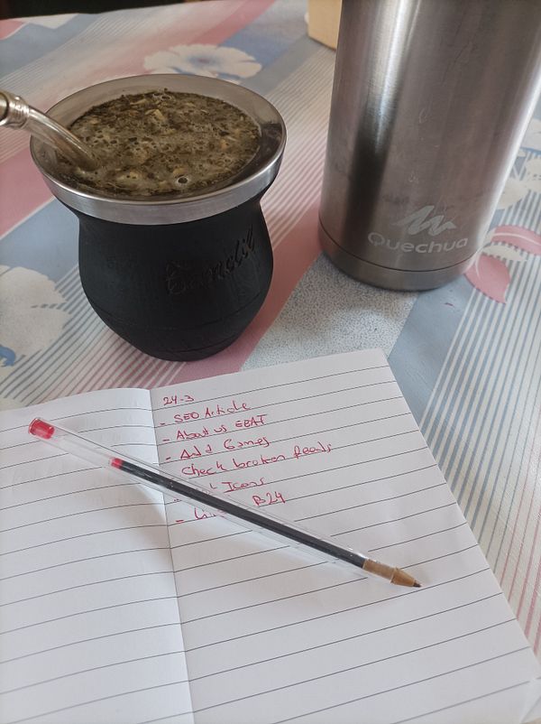 A workspace featuring a traditional mate drink, a notebook with tasks, and a thermos.