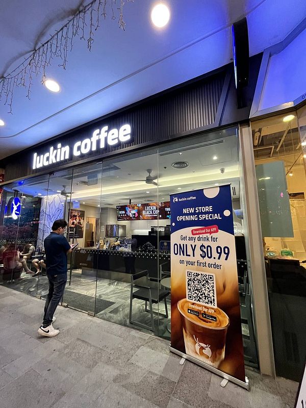 A storefront of Luckin Coffee featuring a promotional banner for a new store opening.
