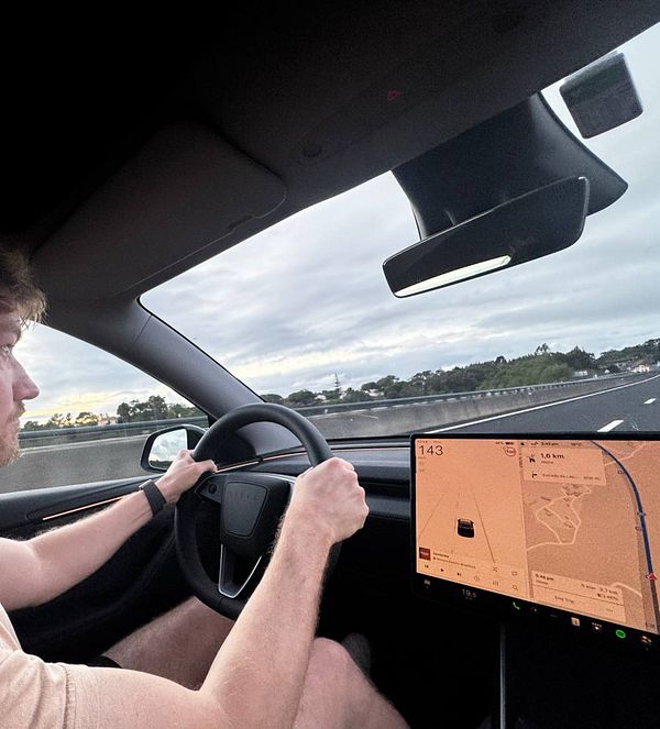 A man is driving a Tesla on a highway with a navigation screen displaying directions.