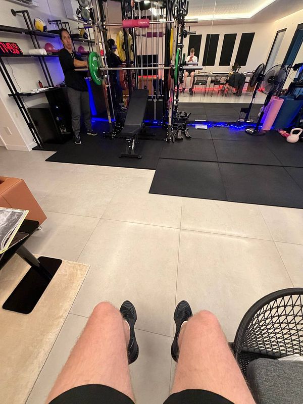 Photograph of a street scene with a gym entrance marked by signage for Planet Fitness and a parking lot with cars.